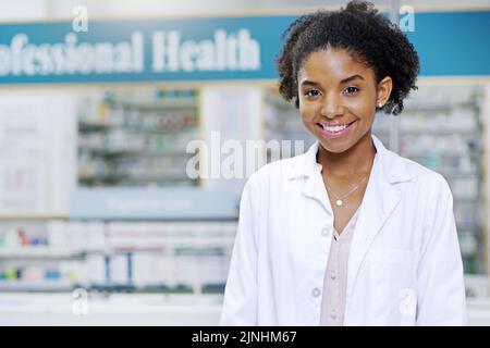 Bei uns steht Ihr Wohlbefinden an erster Stelle. Porträt eines attraktiven jungen Apothekers, der lächelt und in einer Apotheke posiert. Stockfoto