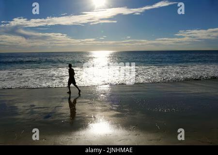 Silhouette eines Mannes, der am Strand in der Nähe des Sonnenuntergangs joggt Stockfoto
