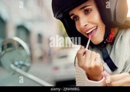 Achten Sie immer darauf, dass Sie auf Reisen vorzeigbar aussehen. Nahaufnahme einer attraktiven jungen Frau, die einen Lippenstift ansetzt, während sie einen Helm trägt Stockfoto