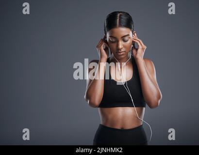 Wählen Sie Musik, die Sie in den richtigen Geisteszustand versetzt. Studioaufnahme einer sportlichen jungen Frau, die vor grauem Hintergrund Musik hört. Stockfoto