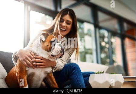 Die besten Menschen im Leben sind Vierbeiner. Eine attraktive junge Frau, die zu Hause auf ihrem Sofa sitzt und mit ihrem Hund spielt. Stockfoto