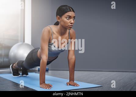 Jede Entscheidung am Ende beinhaltet Balance und Opferbereitschaft. Eine attraktive junge Frau macht zu Hause Stretching-Übungen auf ihrer Fitnessmatte. Stockfoto