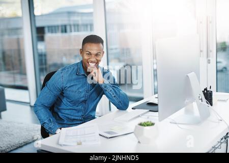 Fordern Sie sich jeden Tag heraus. Porträt eines jungen Geschäftsmannes, der gut gelaunt an seinem Schreibtisch posiert. Stockfoto