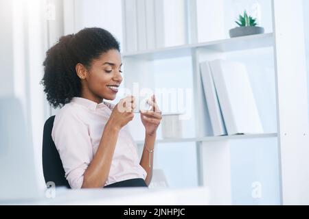 Kaffee inspiriert mich. Eine junge Geschäftsfrau, die in einem Büro eine Tasse Kaffee trinkt. Stockfoto