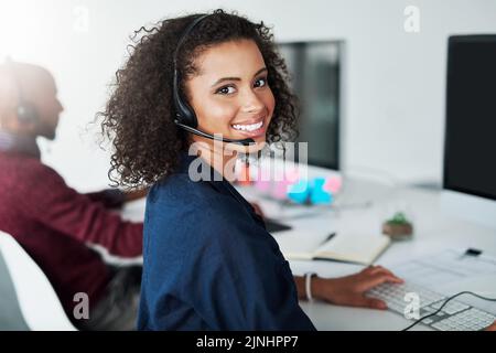 Lassen Sie uns Ihnen helfen. Beschnittenes Porträt einer attraktiven jungen Callcenter-Agenten, die in ihrem Büro arbeitet. Stockfoto