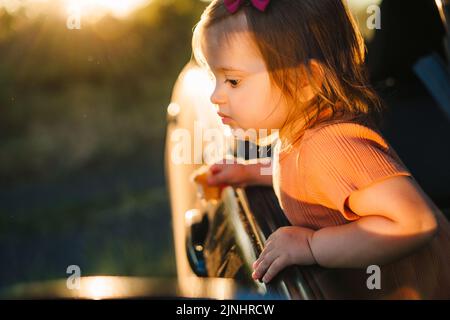Baby Mädchen aus Auto-Fenster schauen und neugierig untersucht die Natur. Familienreise mit dem Auto in den Bergen. Kleines Kind, das mit dem Auto unterwegs ist. Kindersicherheit Stockfoto