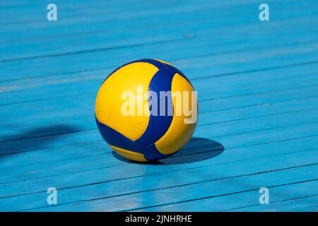 Gelb-Volleyball auf einem Volleyballplatz. Der Boden ist aus Holz und mit blauer Farbe bedeckt. Stockfoto