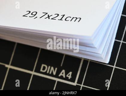 Karlsruhe, Deutschland. 08. August 2022. In einer Druckerei liegen A4 Blatt Papier auf einer Papierschneidemaschine. Auf dem Deckblatt ist 29,7 x 21 Zentimeter gedruckt. Die berühmtesten 29,7 mal 21 Zentimeter werden 100 Jahre alt, das Format DIN A4. Am 18. August 2022, also vor genau 100 Jahren, hat das Deutsche Institut für Normung (DIN) seine Richtlinie 476 für Papierformate veröffentlicht. Seitdem sind der Typ A4 und seine Geschwister das Maß aller Dinge in Büro und Schule. Quelle: Uli Deck/dpa/Alamy Live News Stockfoto