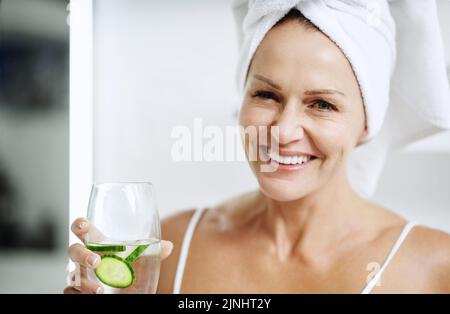 Probieren Sie es einfach aus, es funktioniert. Eine reife Frau hält ein Glas Wasser mit Gurke in sich. Stockfoto