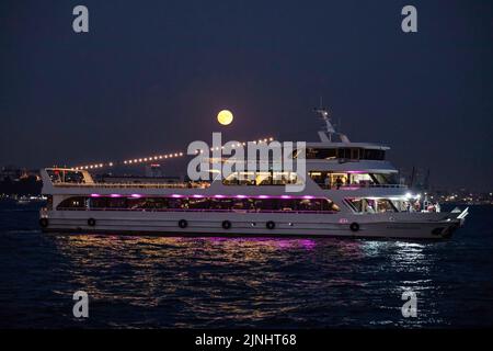 Istanbul, Türkei. 11. August 2022. Ein Kreuzfahrtboot am Bosporus mit Vollmond am Himmel. Boote, die durch den Bosporus und die Stadtlinien-Fähren fuhren, wurden in Istanbul gesehen, wobei der Vollmond am Himmel in den Abendstunden erschien. Kredit: SOPA Images Limited/Alamy Live Nachrichten Stockfoto