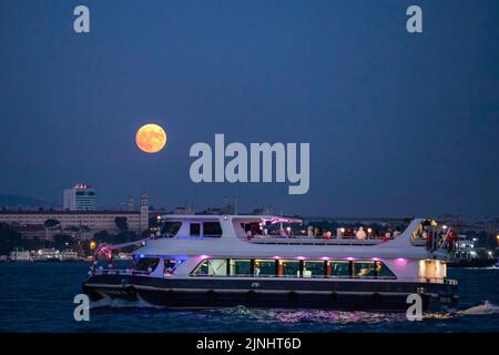 Istanbul, Türkei. 11. August 2022. Ein Kreuzfahrtboot am Bosporus mit Vollmond am Himmel. Boote, die durch den Bosporus und die Stadtlinien-Fähren fuhren, wurden in Istanbul gesehen, wobei der Vollmond am Himmel in den Abendstunden erschien. Kredit: SOPA Images Limited/Alamy Live Nachrichten Stockfoto