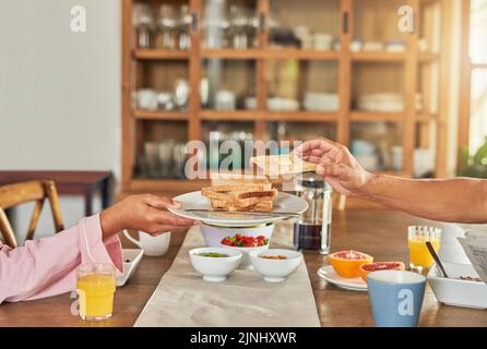 Eine unkenntliche Frau, die einem Mann während des Frühstücks zu Hause einen Teller Toast überreichte. Stockfoto