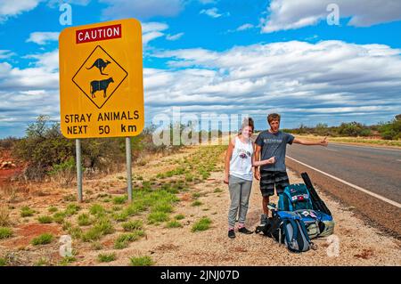 Ein paar junge britische Rucksacktouristen warten auf einen Aufzug auf der Autobahn in der Nähe von Monkey Mia in Westaustralien Stockfoto