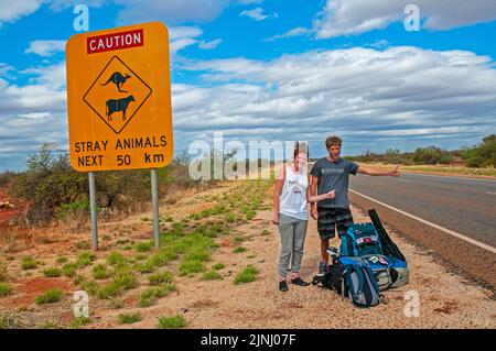 Ein paar junge britische Rucksacktouristen warten auf einen Aufzug auf der Autobahn in der Nähe von Monkey Mia in Westaustralien Stockfoto