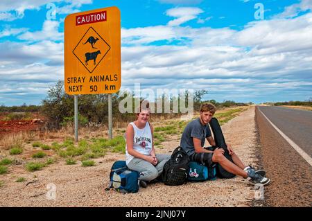 Ein paar junge britische Rucksacktouristen warten auf einen Aufzug auf der Autobahn in der Nähe von Monkey Mia in Westaustralien Stockfoto