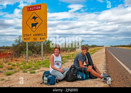 Ein paar junge britische Rucksacktouristen warten auf einen Aufzug auf der Autobahn in der Nähe von Monkey Mia in Westaustralien Stockfoto