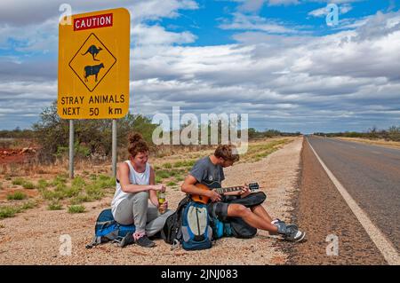 Ein paar junge britische Rucksacktouristen warten auf einen Aufzug auf der Autobahn in der Nähe von Monkey Mia in Westaustralien Stockfoto