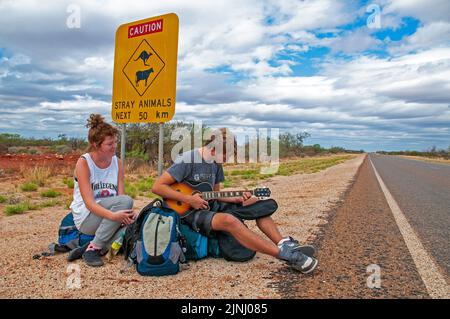 Ein paar junge britische Rucksacktouristen warten auf einen Aufzug auf der Autobahn in der Nähe von Monkey Mia in Westaustralien Stockfoto