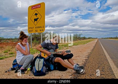 Ein paar junge britische Rucksacktouristen warten auf einen Aufzug auf der Autobahn in der Nähe von Monkey Mia in Westaustralien Stockfoto