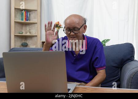 Asiatischer älterer Mann, der zu Hause auf dem Computer mit Videoanruf und Internetkommunikation sitzt. Stockfoto