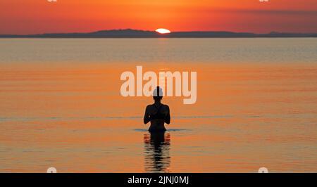 Portobello, Edinburgh, Schottland, Großbritannien. 12.. August 2022. Atemberaubender Sonnenaufgang, um eine sehr heiße Woche mit überdurchschnittlichen Temperaturen für Schottland zu beenden, Temperatur heute Morgen im Morgengrauen 13 Grad Celsius für diejenigen, die am Firth of Forth Seaside Sport treiben wollen, wobei haar später an der Ostküste erwartet wird. Im Bild: Diese junge Frau genießt ein kaltes Wasserbad in der Morgendämmerung, gerade als die Sonne beginnt, über den Horizont zu blicken. Quelle: Arch White/alamy Live News. Stockfoto