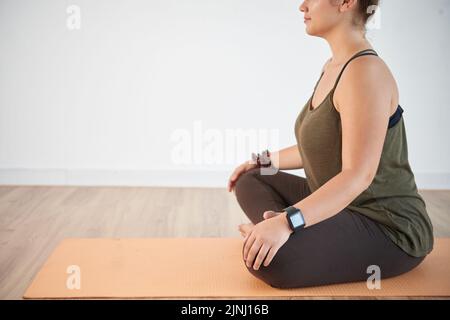 Profilansicht einer selbstbewussten jungen Frau, die in Lotusposition sitzt, während sie im modernen Health Club trainiert, Kopierraum Stockfoto