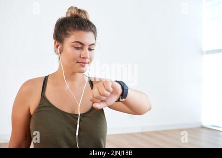 Selbstbewusste, sportliche Frau, die mithilfe der Smartwatch die Herzfrequenz überprüft und gleichzeitig im modernen Health Club intensiv trainiert, Porträtaufnahme Stockfoto