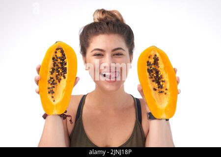 Kopf- und Schulterporträt einer attraktiven jungen Frau, die reife Papaya-Hälften in den Händen hält und Lippen leckt, isoliert auf weißem Hintergrund Stockfoto