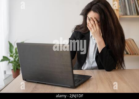 Frau, die im Büro am Laptop arbeitet, Kopfschmerzen, Migräne, Stressabbau, chronische Schmerzen, helfen bei der Beruhigung. Chronisches Erschöpfungssyndrom Stockfoto