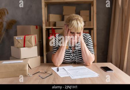 Ältere gestresste Geschäftsfrau sitzend und den Kopf mit schmerzenden Gesichtsausdruck berührend. Geschäftsperson, die Schmerzen spürt, an Migräne leidet, überfordert Stockfoto