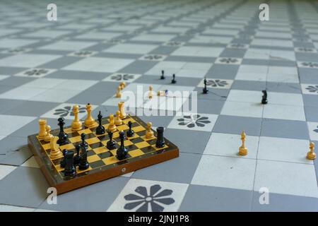 Schachbrett mit verstreuten Figuren steht auf kariertem Boden. Hochwertige Fotos Stockfoto