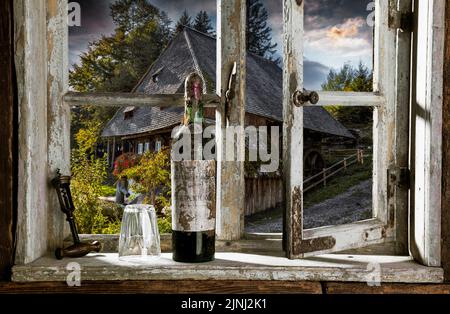 Blick durch rustikales Holzfenster mit alter Weinflasche auf eine historische Wassermühle Stockfoto