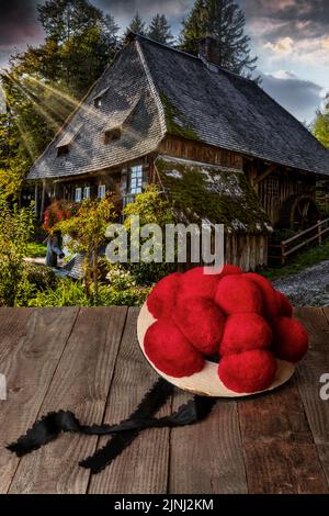 Original Schwarzwälder Bollenhut auf einem Holztisch vor einer historischen Wassermühle Stockfoto