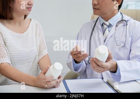 Selbstbewusster Arzt mittleren Alters mit weißem Mantel am Schreibtisch sitzend und jungen Patienten Pillen verordnet, Nahaufnahme Stockfoto