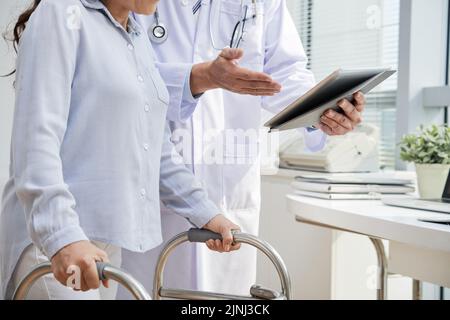 Nahaufnahme eines männlichen Physiotherapeuten mit weißem Mantel mit digitalem Tablet, während er sich mit einem Traumatize-Patienten betraumatisiert Stockfoto