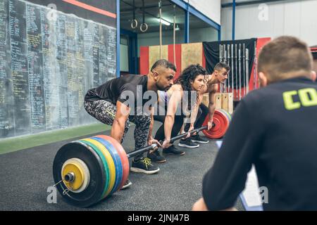 Gemischtes Team, das mit dem Trainer Gewichte im Fitnessstudio hebt Stockfoto