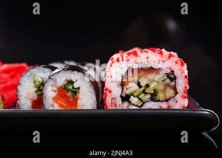 Reis Japanische Rollen von Uramaki und Maki mit Lachs, Gurke und rotem Kaviar auf einem schwarzen Teller. Traditionelle japanische Küche. Nahaufnahme. Stockfoto