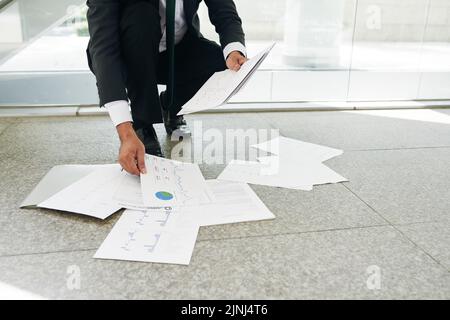 Nicht erkennbarer Geschäftsmann, der Dokumente abholt, die auf dem Boden gefallen sind Stockfoto