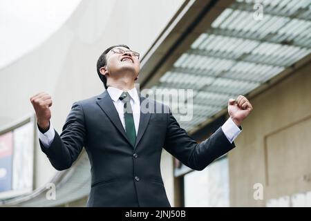 Ekstatischer asiatischer Geschäftsmann feiert Erfolg im Bürogebäude Stockfoto