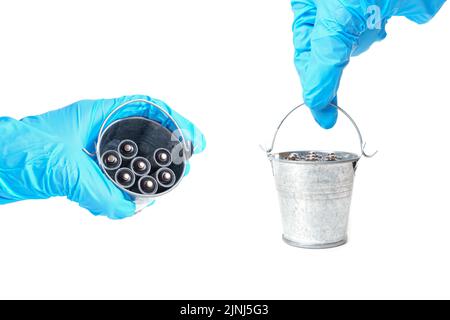 Handschuh, der einen kleinen Stahleimer voll stark korrodierter gebrauchter AA-Batterien auf Weiß hält. Stockfoto