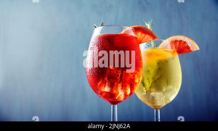 Schleppgläser aus rotem und gelbem aperol Spritz Cocktail mit Rosmarin und Grapefruit auf blauem Hintergrund. Sommerparty Happy Hour Restaurant Bar-Menü. Ita Stockfoto