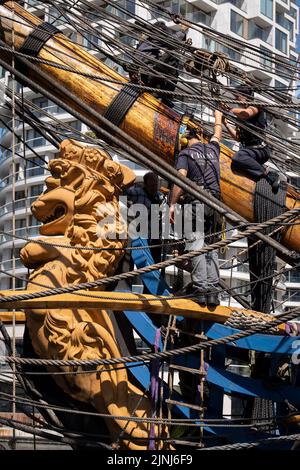 Crew-Mitglieder des nachgebauten Segelschiffs Gotheborg führen Reparaturen und Wartungsarbeiten am Galionsschiff des Schiffes durch, während sie während ihres viertägigen Besuchs in der Hauptstadt unter den Hochhäusern am South Quay, Canary Wharf in den Londoner Docklands, andockten, bevor es seine zweijährige Weltexpedition nach Shanghai, China, fortsetzt. Am 9.. August 2022 in London, England. Londoners sind eingeladen, die Decks dieses Faksimiliers des ursprünglichen Schiffes zu besichtigen, das 1745 vor der schwedischen Küste sank. Die Hauptfracht wäre Tee, Porzellan, Kräuter und Seide auf der China-Route gewesen. Stockfoto