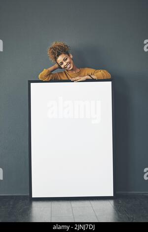 Eine schöne selbstbewusste Frau, die ein leeres Whiteboard oder ein Plakatschild mit Kopierfläche hält. Glückliche und attraktive Frau mit einem Lächeln hinter einem Stockfoto