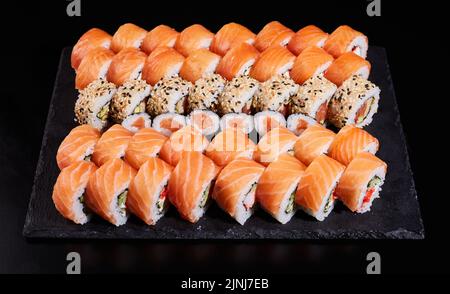 Sushi-Set, das aus einer großen Anzahl von Rollen von Philadelphia mit rohem Lachs und anderen Sushi dazwischen besteht. Japanisches Sushi-Set. Verschiedene Arten von Stockfoto