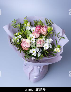 Draufsicht auf einen Strauß von Rosen und grünen Zweigen auf blauem Hintergrund. Festlich gepackter Strauß mit rosa Rosen, weißen Chrysanthemen und gree-Zweige Stockfoto