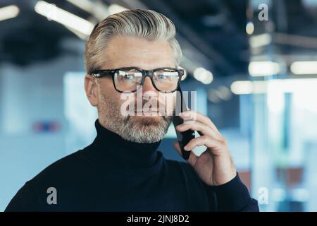 Nahaufnahme Porträt des denkenden älteren grauhaarigen Geschäftsmann Mann in der Brille nachdenklich reden am Telefon und Blick auf die Kamera, erfolgreiche Investor bei der Arbeit in der Mitte eines modernen Büros Stockfoto
