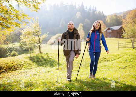 Mann und Frau mit Rucksäcken auf den Schultern und mit Trekkingstöcken wandern in den Bergen. Das Paar führt einen aktiven und gesunden Lebensstil zusammen Stockfoto