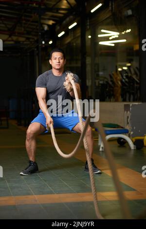 Hübsche junge Frau, die im Fitnessstudio mit Kampfseilen trainieren kann Stockfoto