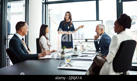 Geschäftsfrau bei einem Investment-Meeting mit Finanzdaten auf einem Bildschirm des Sitzungssitzes. Internationales Führungsteam hört sich eine Präsentation an Stockfoto