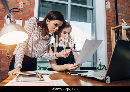 Zwei junge Frauen, die im Büro mit Dokumenten arbeiten. Stockfoto